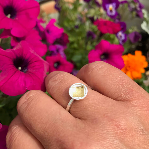 close up of sterling silver gold ring on hand with flowers in the background