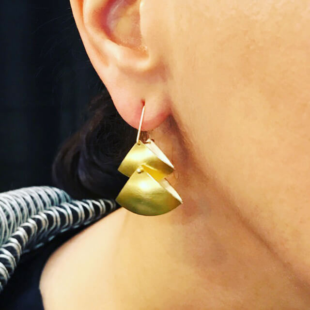 close up of gold fan earrings on woman