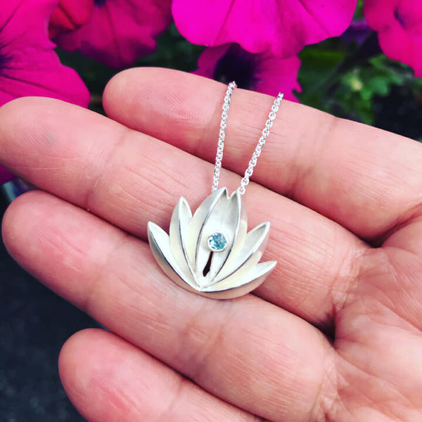 close up of lotus pendant on hand with flowers in background